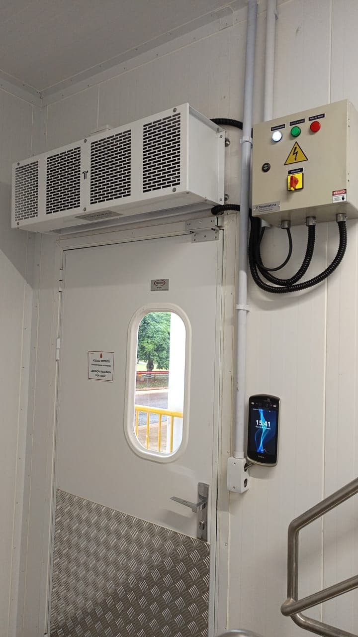 Cortina de ar Tecnolatina instalada sobre porta industrial ao lado do painel elétrico de comando