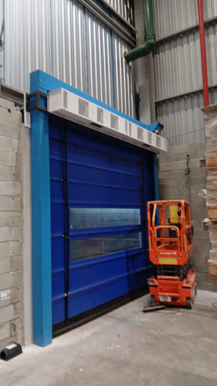 Cortina de ar industrial instalada sobre uma porta rápida azul em uma indústria de embalagens