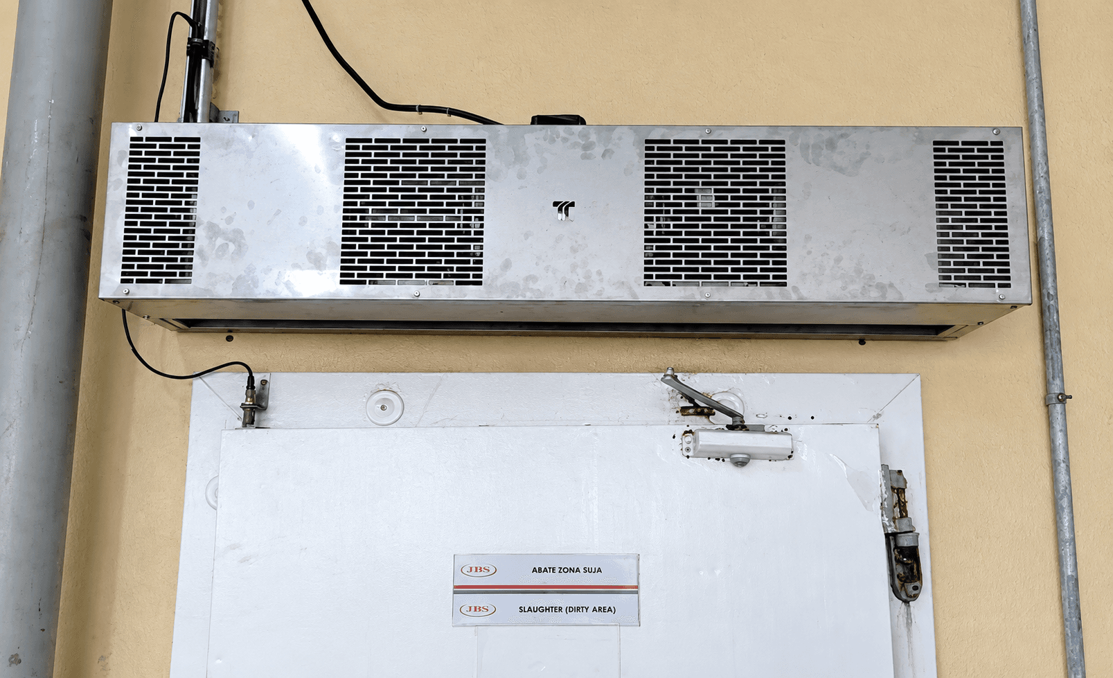 Cortina de ar metálica fixada na parede acima de porta industrial branca