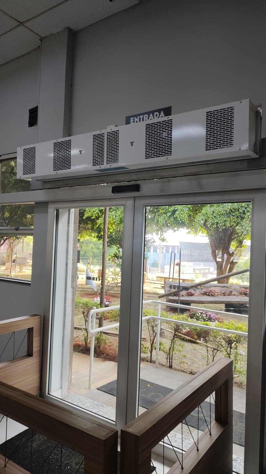 Cortinas de ar brancas instaladas acima de porta de vidro sinalizada como entrada