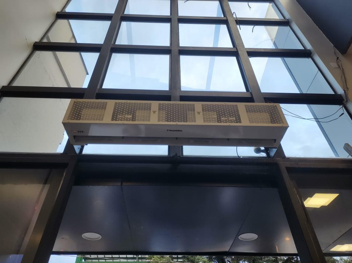 Cortina de ar instalada sobre entrada com estrutura metálica e painéis de vidro