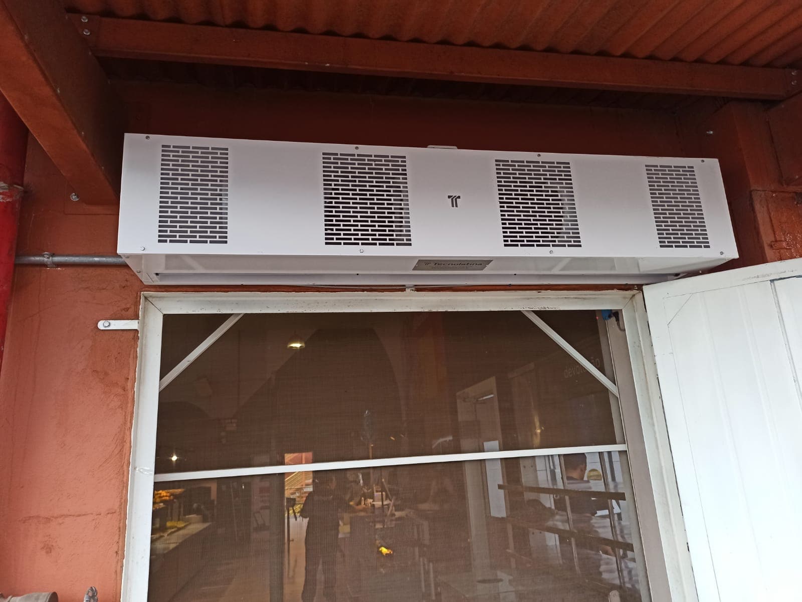 Cortina de ar branca sobre porta em parede avermelhada sob cobertura
