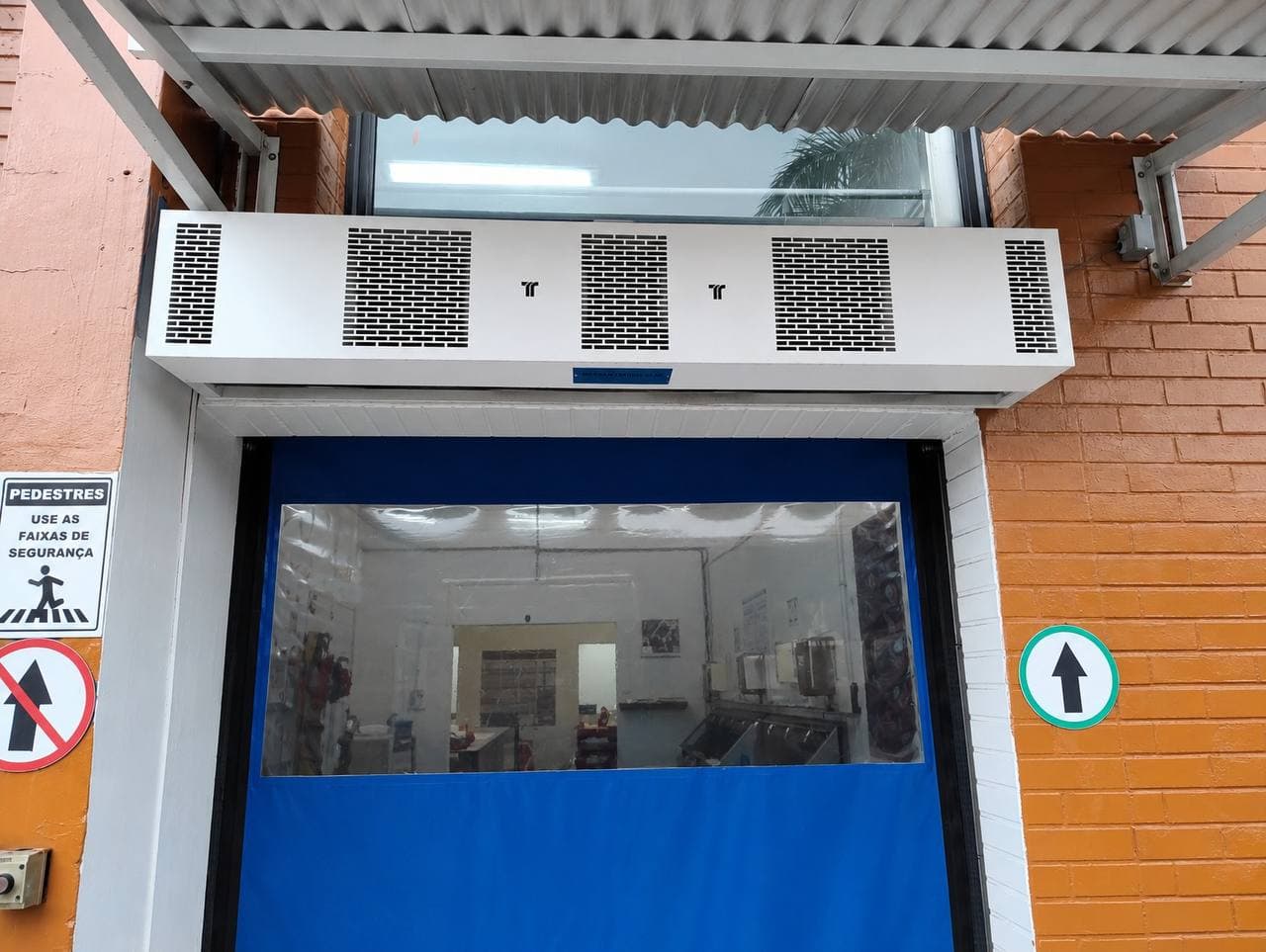 Cortina de ar branca acima de porta rápida azul em parede de tijolos