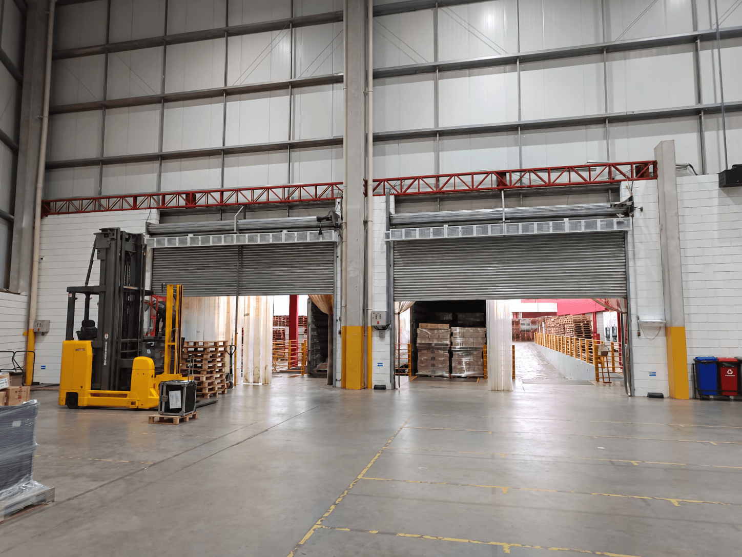 Cortinas de ar acima de duas portas industriais, com empilhadeira à esquerda; foto tratada digitalmente