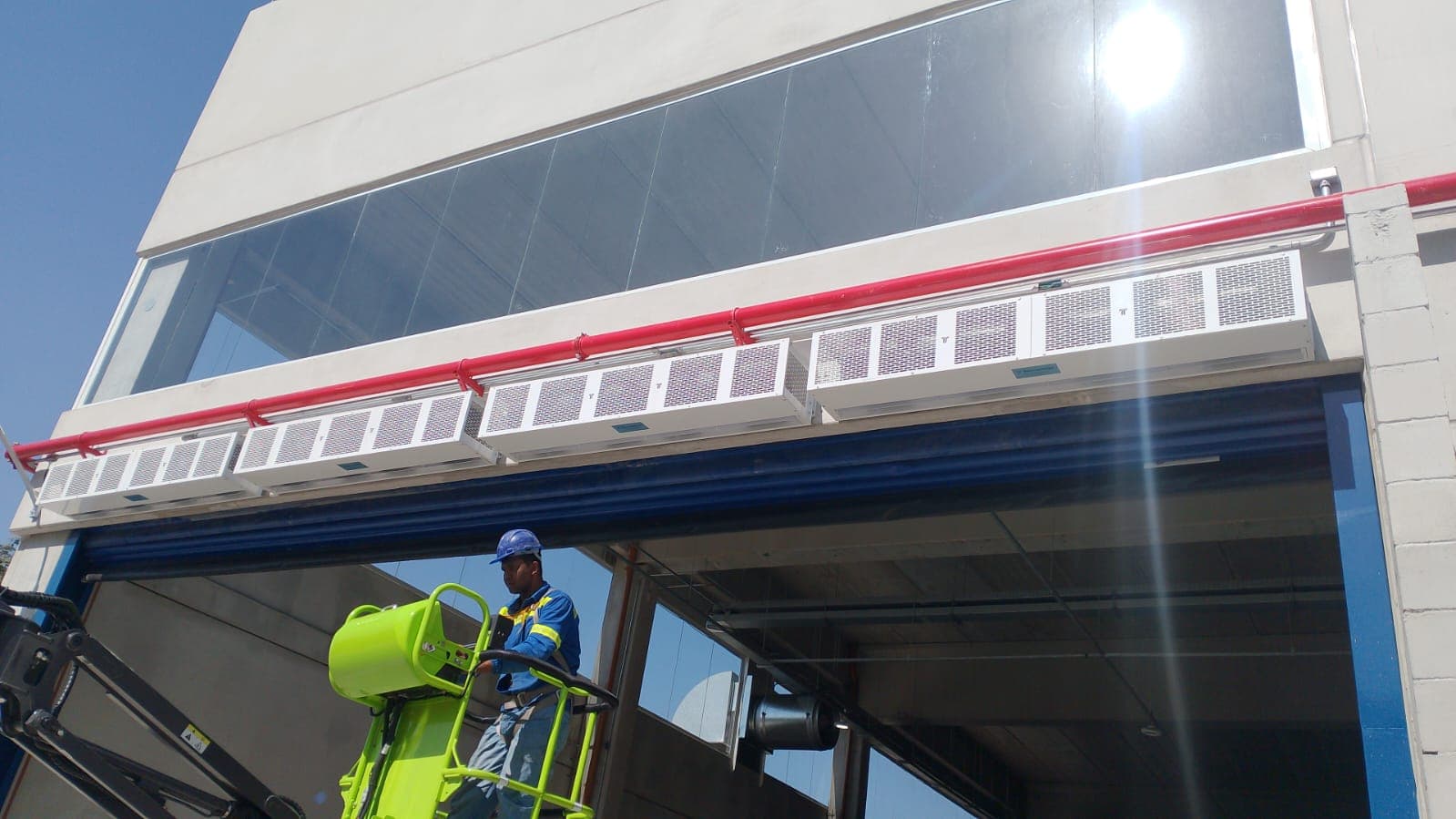 Cortinas de ar brancas alinhadas acima de abertura industrial, com profissional em plataforma