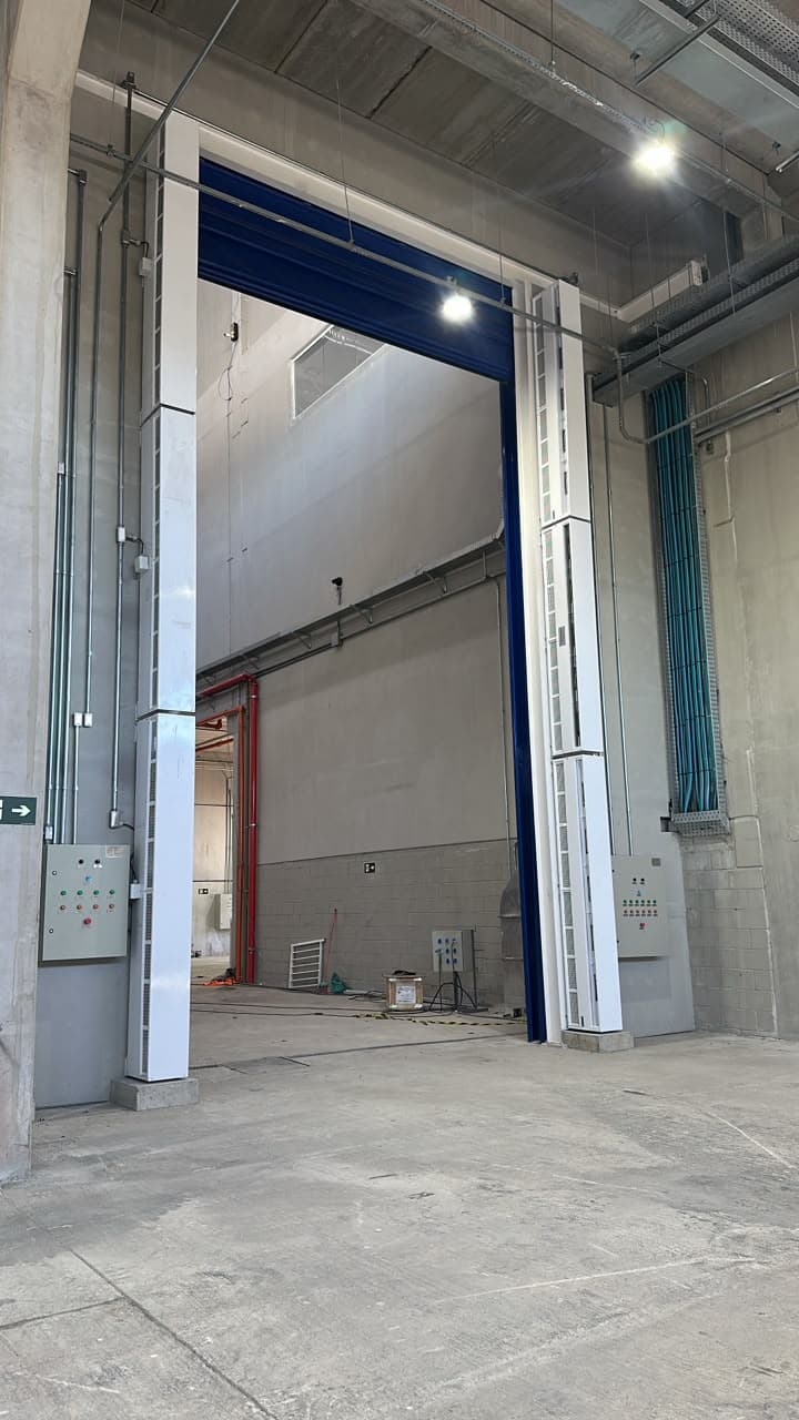 Porta rápida azul aberta com cortinas de ar verticais e painéis de comando nos dois lados do vão
