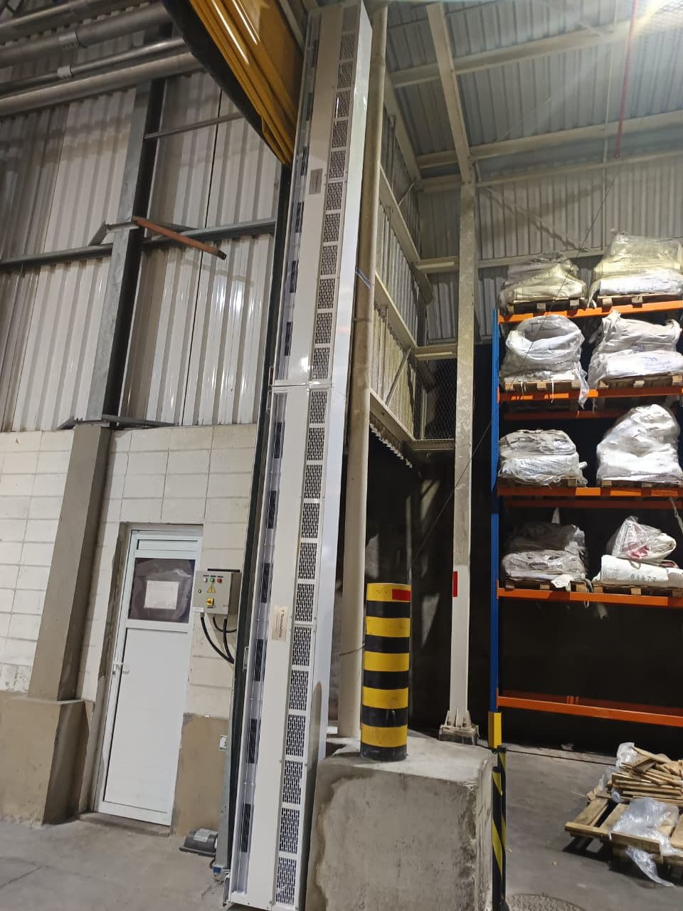 Cortina de ar vertical fixada junto ao acesso de galpão com prateleiras de armazenagem
